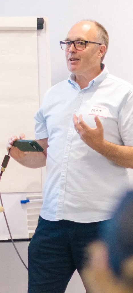 Mat Bennett speaking to a room of agency founders, holding notes beside a flipchart.